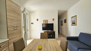 A modern living room with a wooden dining table, a sofa, and a TV on a stand.