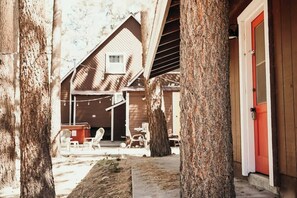 A rustic wooden building with a red door, surrounded by trees and outdoor seating. - Bearadise • Spa • Gameroom • Walk to Lake • Fenced (Big Bear Lake)
