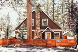 A cabin with a stone chimney, wooden exterior, and a fenced yard. - Bearadise • Spa • Gameroom • Walk to Lake • Fenced (Big Bear Lake)