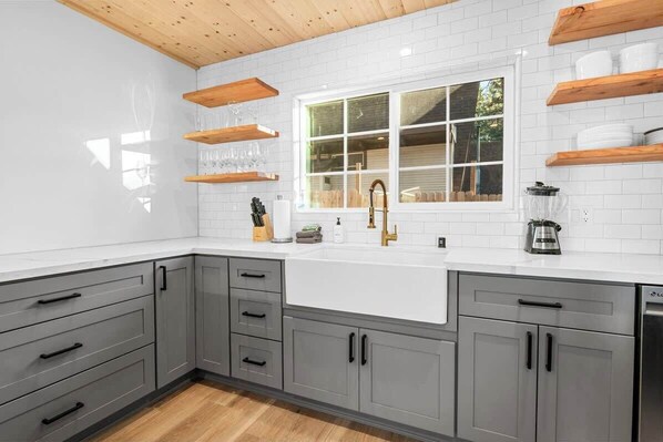 Una cocina moderna con armarios grises, encimera blanca y estantes de madera.