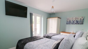 A bedroom with two beds, a TV, a wardrobe, and a painting. - Meadowbank Lodge (Driffield)