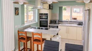 A compact kitchen with a central island, wooden chairs, a sink, and a window with a view of a wooden fence. - Meadowbank Lodge (Driffield)