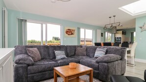 A modern living room with a sectional sofa, a wooden coffee table, and a dining area in the background. - Meadowbank Lodge (Driffield)