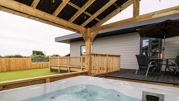 A hot tub on a wooden deck with a view of a house and a grassy yard. - Meadowbank Lodge (Driffield)