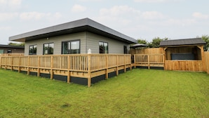 A modern house with a flat roof, large windows, and a wooden deck. - Meadowbank Lodge (Driffield)