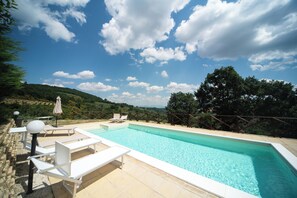 A swimming pool with lounge chairs and a view of a hilly landscape.