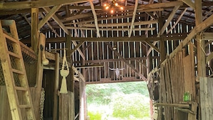 A rustic barn interior with a wooden ceiling, a hanging light fixture, and a gravel floor.