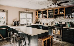 A kitchen with a central island, bar stools, a stove, and a ceiling fan.