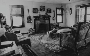 A room with a fireplace, a guitar, and various framed pictures on the wall.