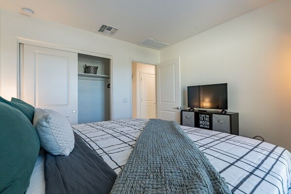 A bedroom with a bed, a television on a stand, and a closet with a basket on the shelf.