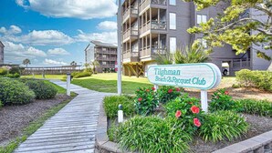 A sign for 'Tilghman Beach & Racquet Club' with a wooden boardwalk leading to a building with balconies. - Oceanfront 3 BR 2.5 bath Tilgham Beach & Racquet Club # 307. 2 pools, Tennis (North Myrtle Beach)