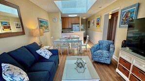 A living room with a sofa, coffee table, TV, and a dining area with chairs and a table. - Oceanfront 3 BR 2.5 bath Tilgham Beach & Racquet Club # 307. 2 pools, Tennis (North Myrtle Beach)