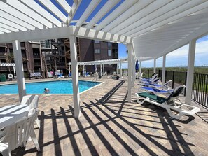 A pool area with a covered deck, lounge chairs, and a view of a building in the background. - Oceanfront 3 BR 2.5 bath Tilgham Beach & Racquet Club # 307. 2 pools, Tennis (North Myrtle Beach)