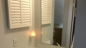 A bathroom with a white sink, a mirror, and a wall-mounted light fixture. - Charming Bungalow suite in Peaceful Sea Palms (St. Simons Island)