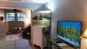 A bedroom with a bed, a desk with a computer, a TV, a fan, and a window. - Charming Bungalow suite in Peaceful Sea Palms (St. Simons Island)