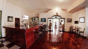 Zona de bar amb un taulell de marbre vermell polit, diverses banquettes i una varietat de botelles i gots.