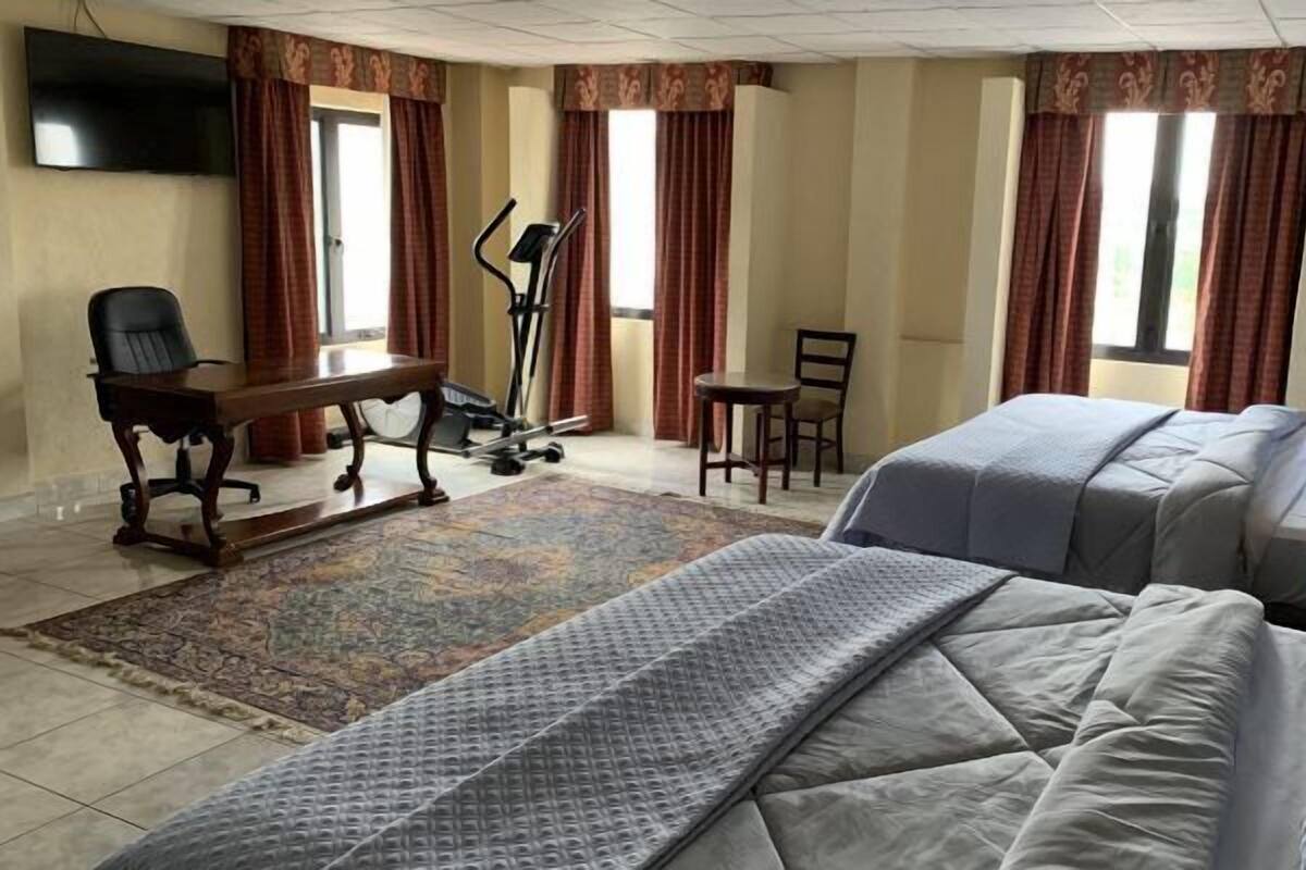 A hotel room with a bed, desk, chair, exercise equipment, and a TV.