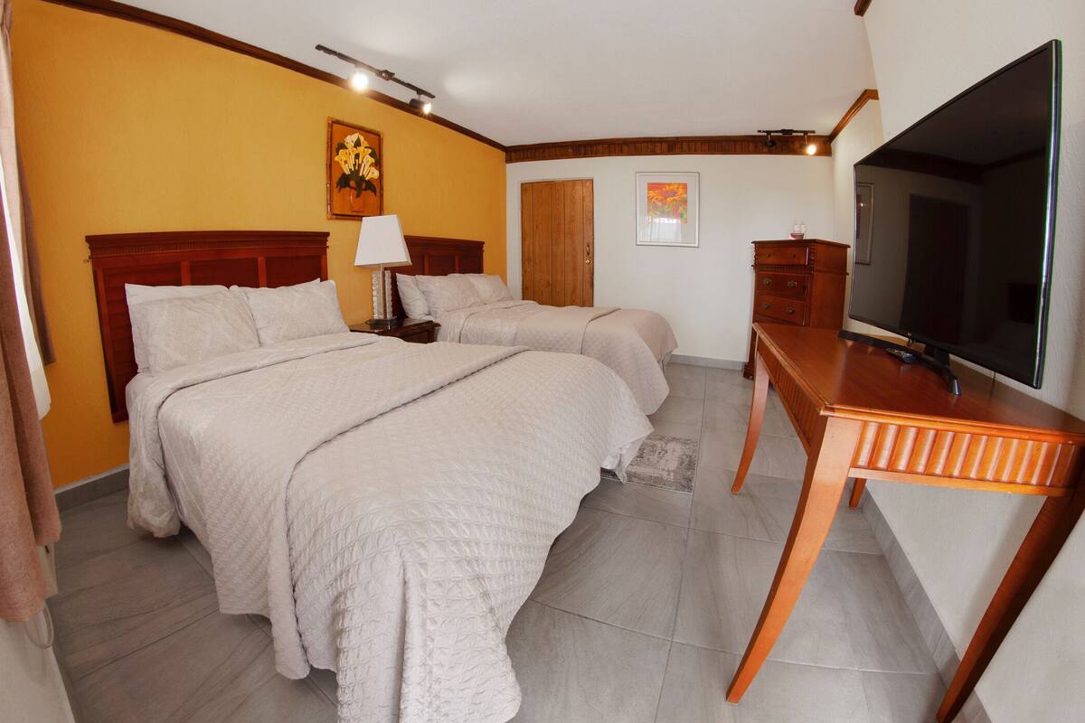 A hotel room with two beds, a desk, a TV, and a wooden headboard.