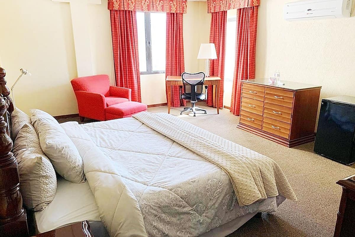 A hotel room with a bed, a red armchair, a desk, and a dresser.