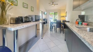 Una cocina moderna con encimera de granito, un comedor con mesa y sillas, y un ventilador de techo.