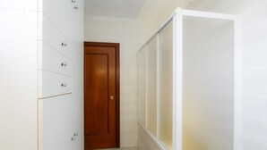 Une salle de bain avec une porte en bois, un meuble blanc doté de plusieurs tiroirs et une cabine de douche en verre.
