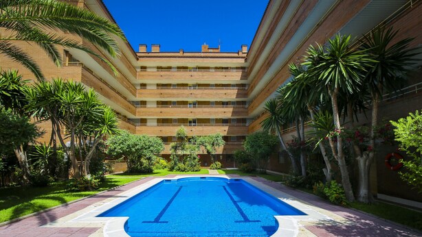 Une piscine entourée de palmiers et un immeuble à plusieurs étages doté de balcons.