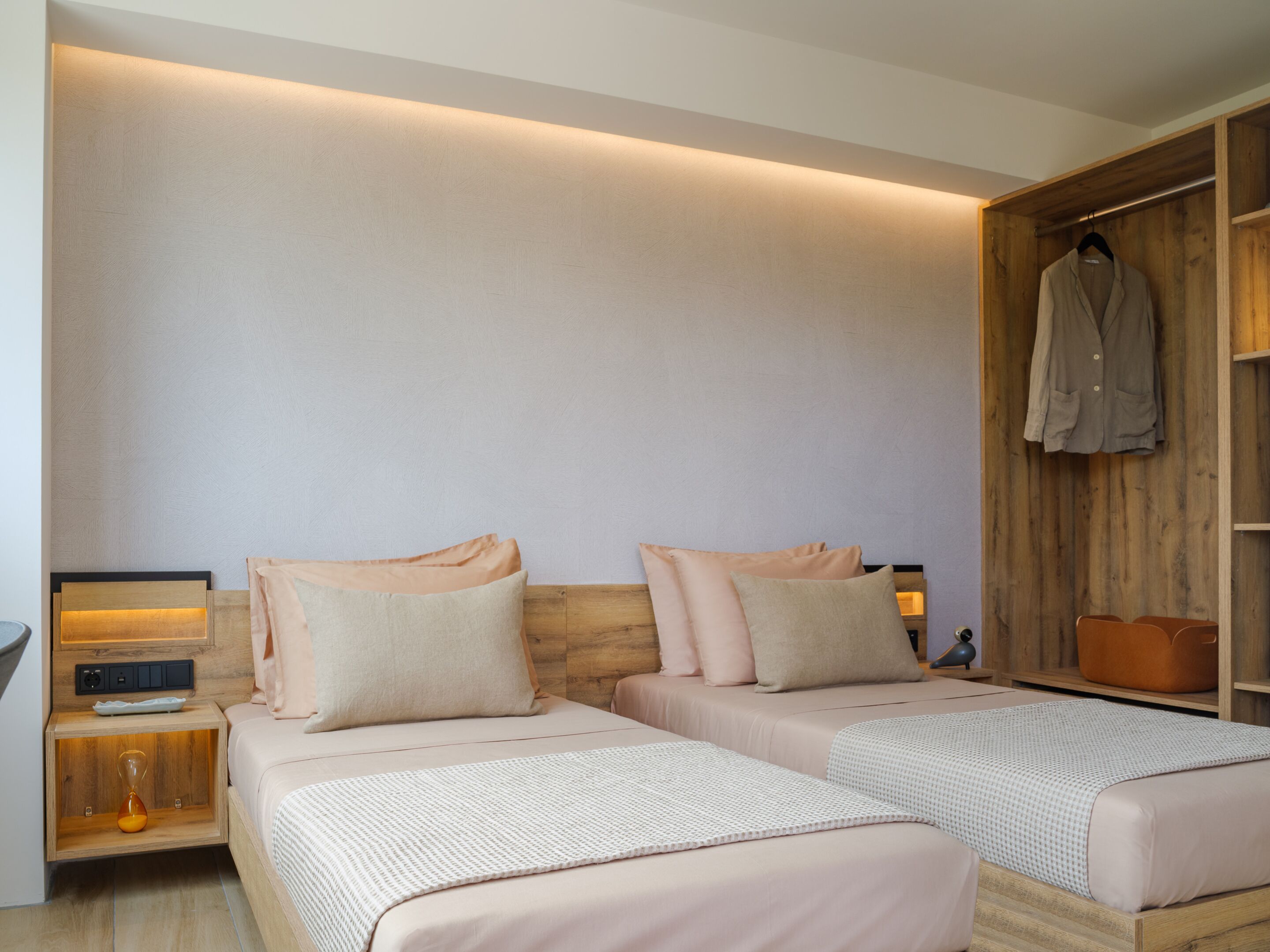 A bedroom with two beds, wooden headboards, bedside tables with lamps, and a wooden wardrobe.
