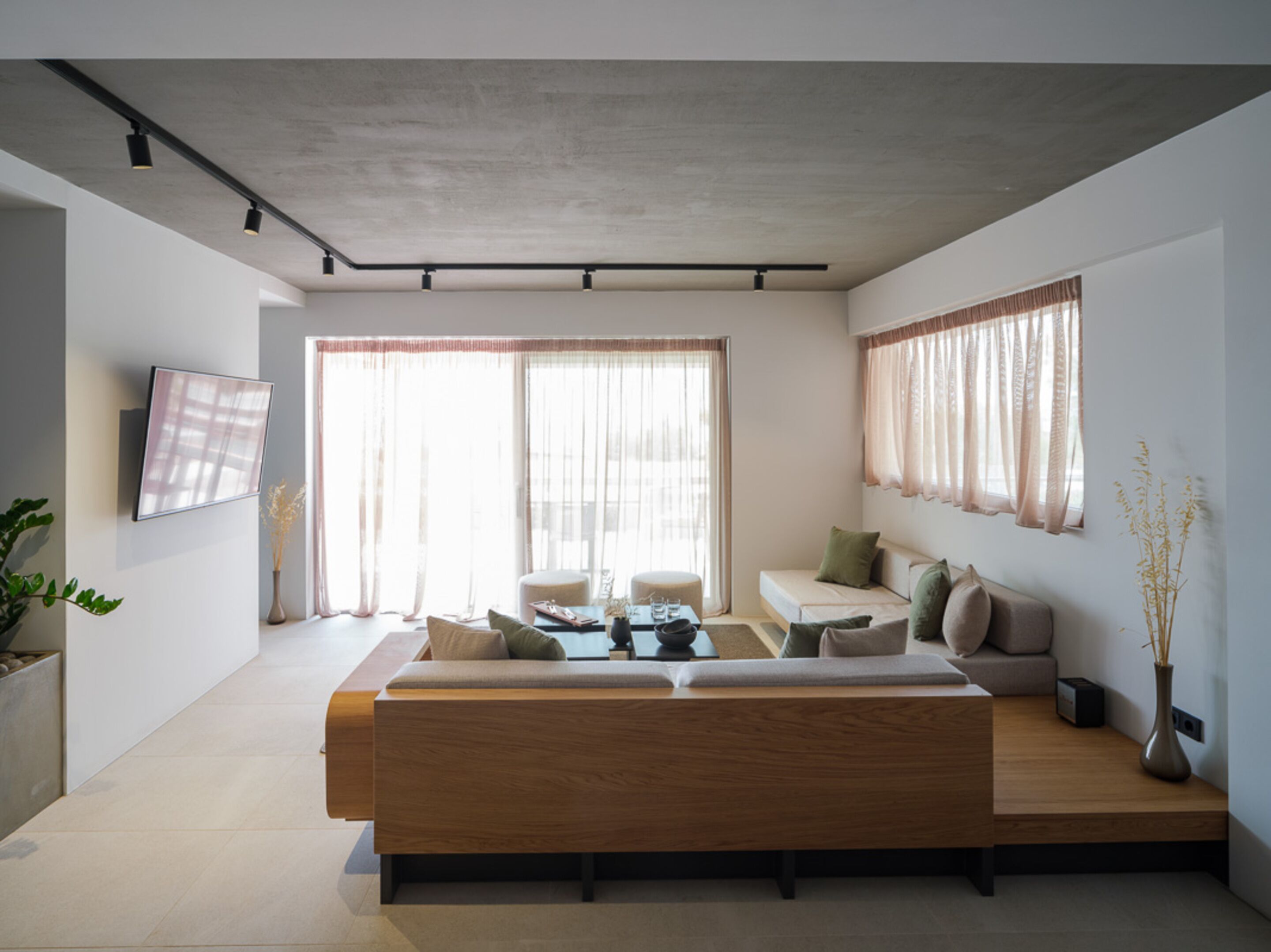 A modern living room with a wooden sofa, a coffee table, and a TV mounted on the wall.