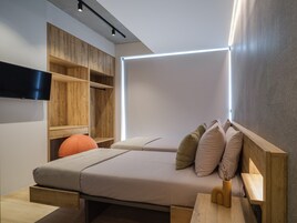 Un dormitorio moderno con cama, almacenaje de madera, un televisor de pantalla plana y una mesita de noche.