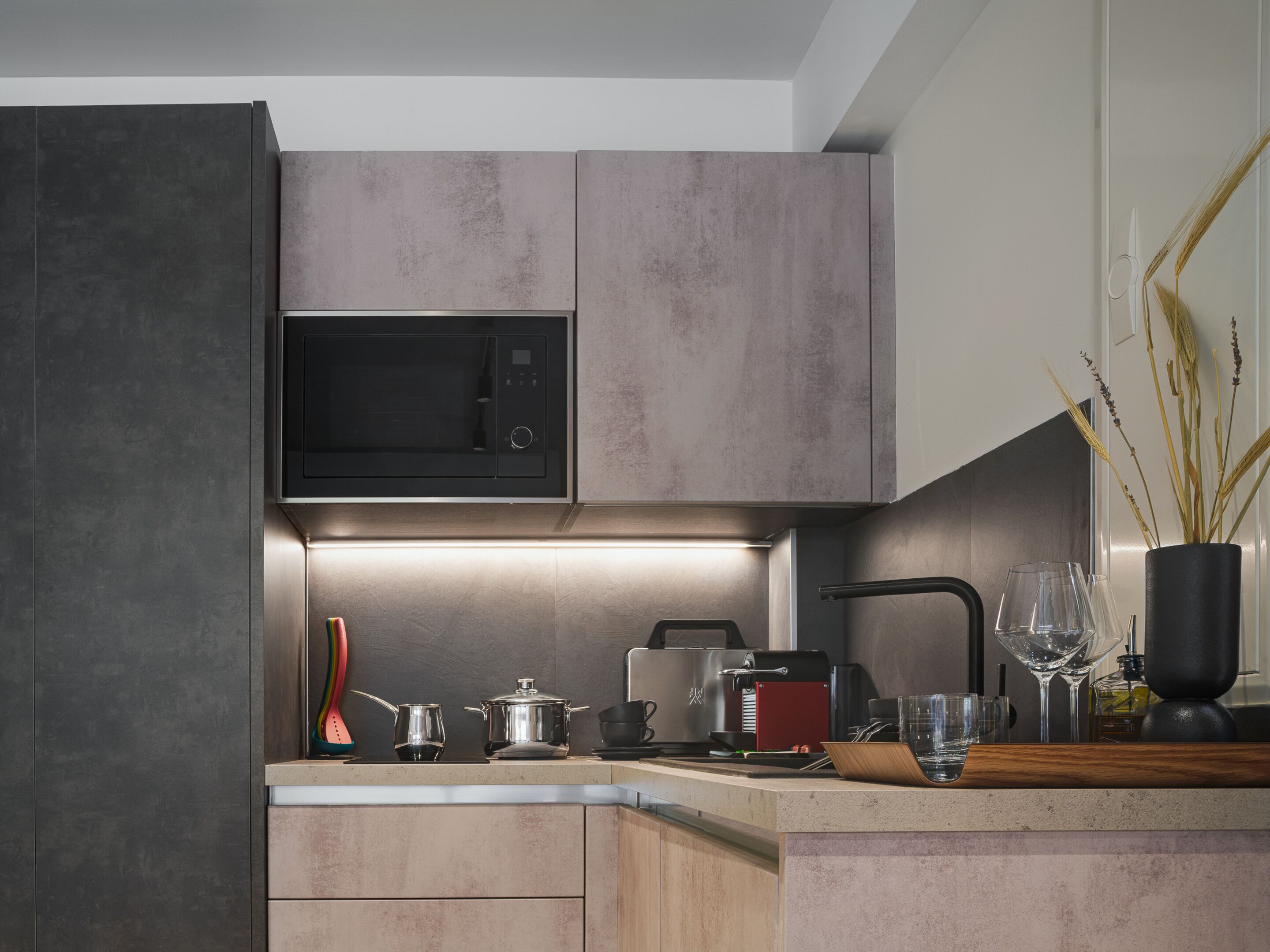 Una cocina moderna con microondas integrado, cafetera y hervidor sobre la encimera.