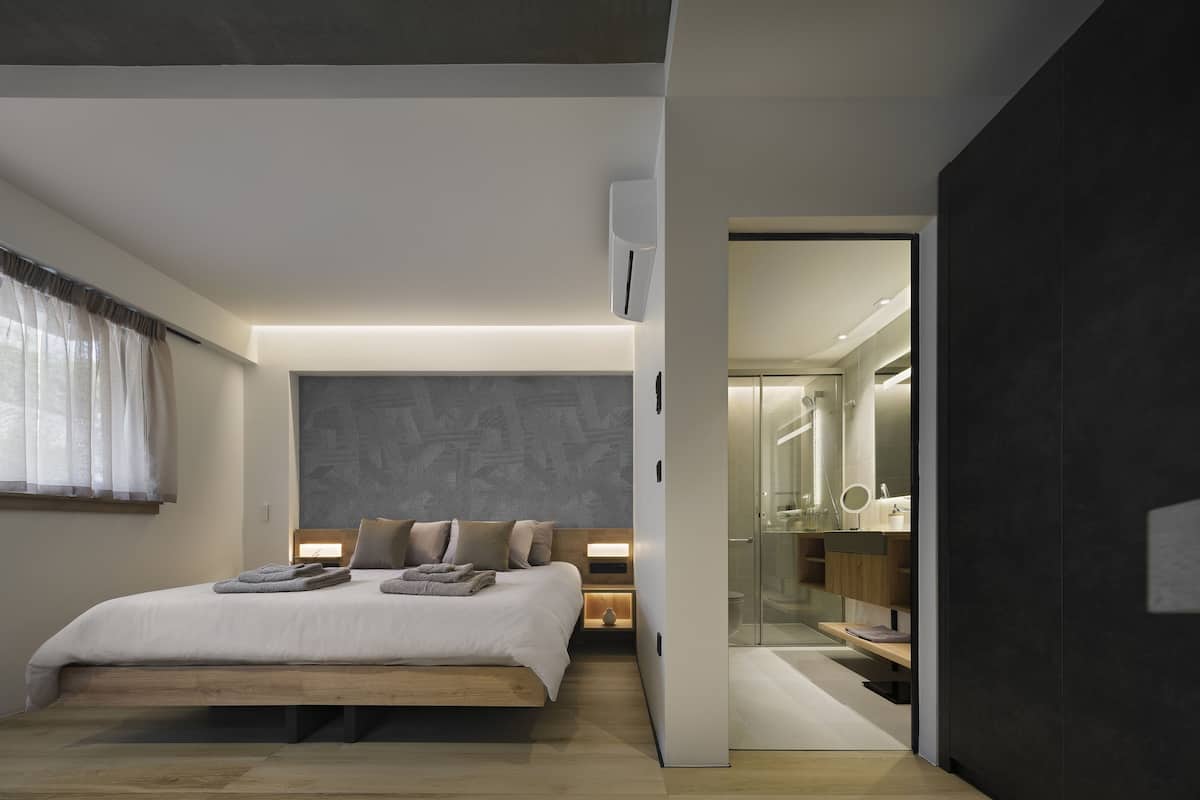 Une chambre moderne avec un grand lit, des lampes de chevet, une douche en verre et un mur d’accent de couleur foncée.