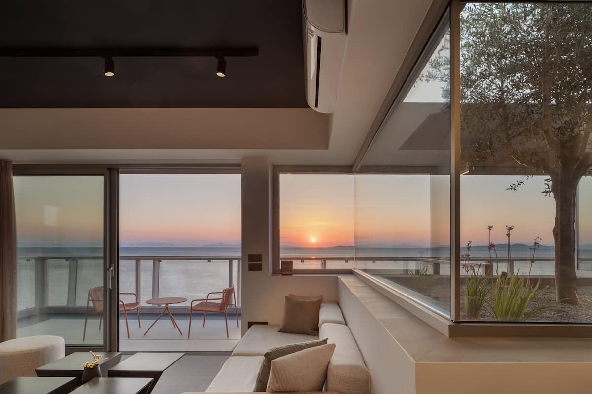 Un salon moderne doté d’une grande fenêtre donnant sur un coucher de soleil sur la mer.