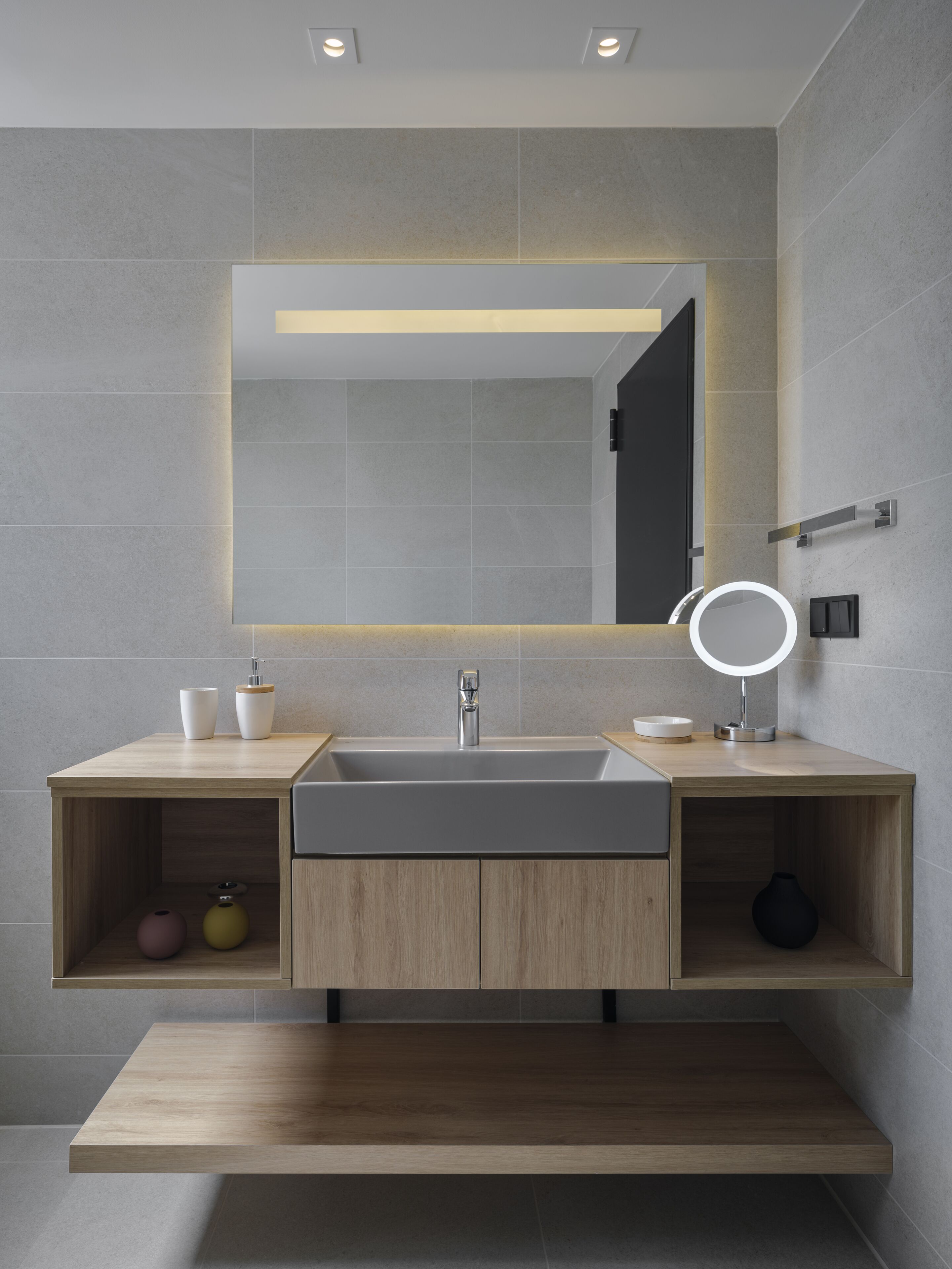A modern bathroom with a large mirror, a sink, and two shelves with toiletries.