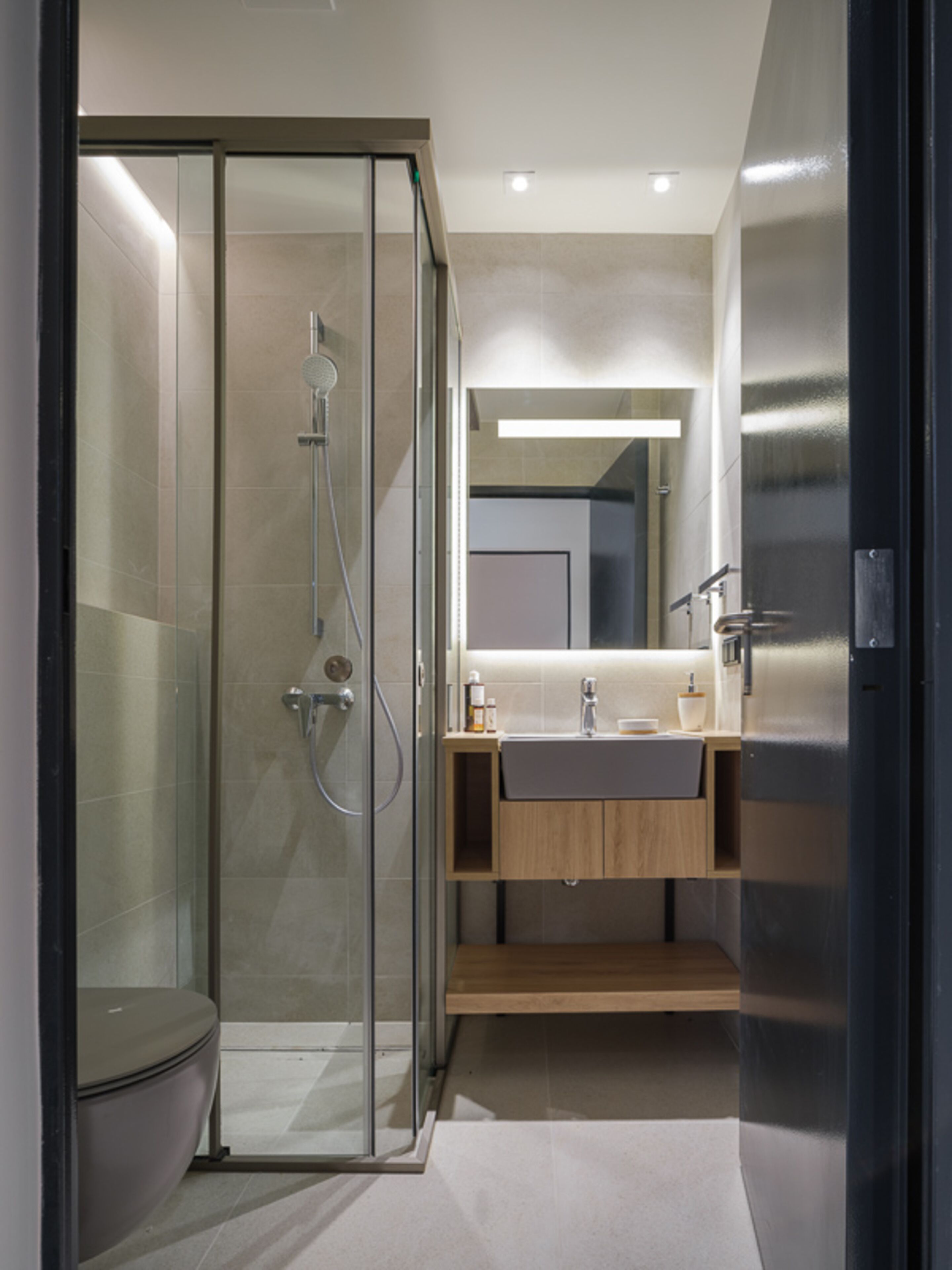 A modern bathroom with a glass-enclosed shower, a toilet, a sink with a mirror, and a wooden cabinet.