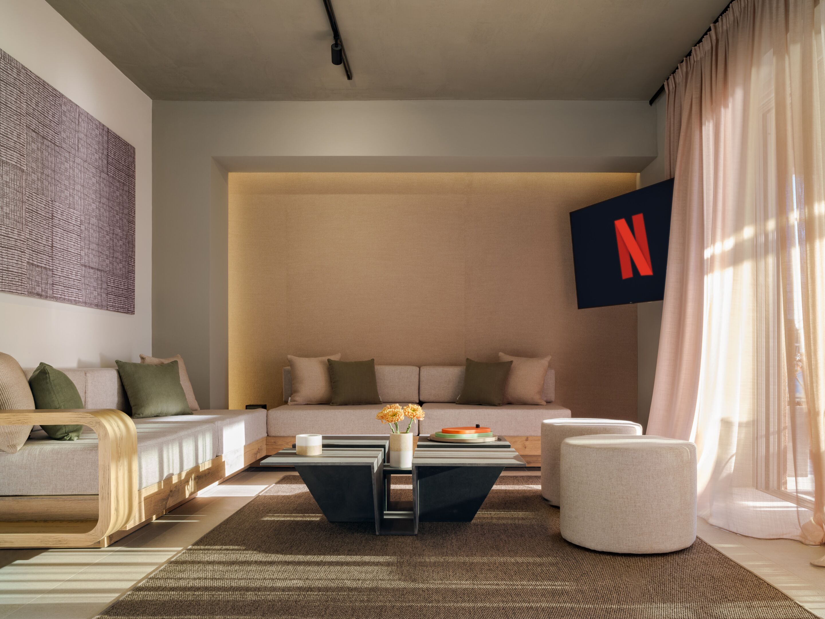 Una sala de estar moderna con sofá, mesa de centro y reposapiés. Se observa un gran logotipo de Netflix en la pared.