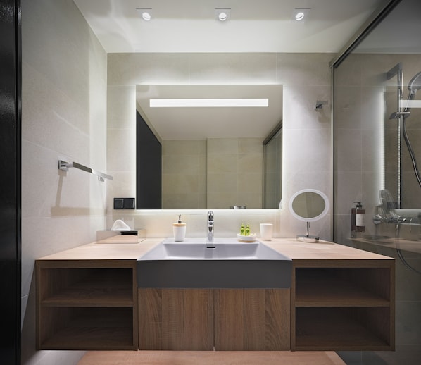 A modern bathroom with a large mirror, two sinks, a shower, and a wooden vanity.