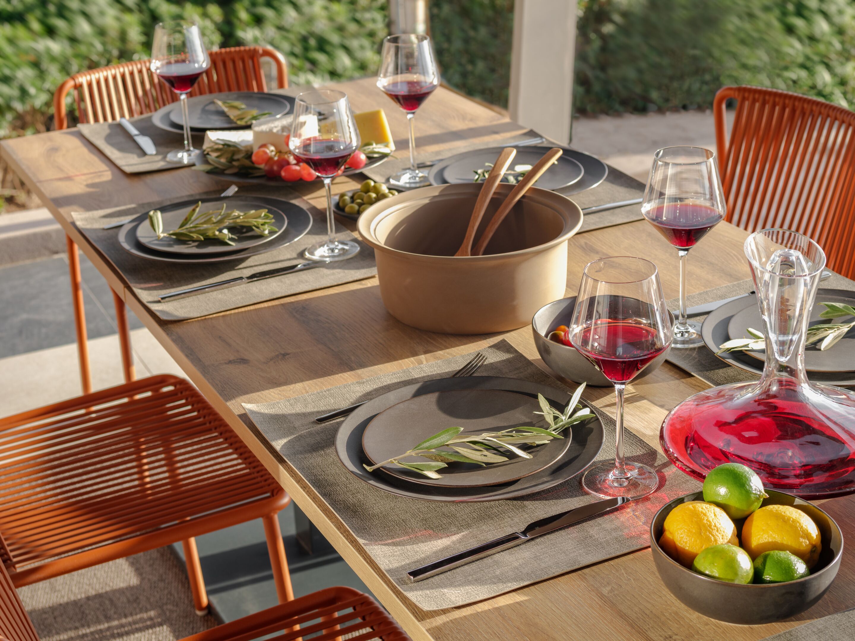 Una mesa de comedor con platos, cubiertos, vasos y un cuenco de fruta.