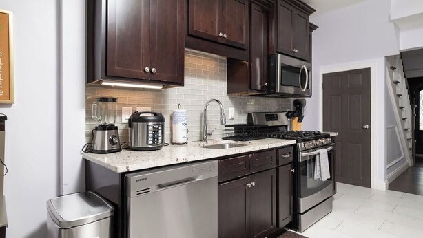 A modern kitchen with dark wooden cabinets, stainless steel appliances, and a white countertop. - Stylish 6-Bedroom Home Near Boston – Dual Units, Yard & Parking Included! (Everett)