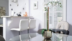 A modern dining area with a glass table, white chairs, and a decorative orchid plant. - Stylish 6-Bedroom Home Near Boston – Dual Units, Yard & Parking Included! (Everett)