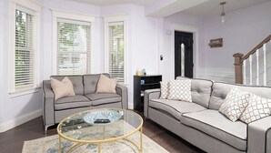 A living room with two sofas, a glass coffee table, and a black bookshelf. - Stylish 6-Bedroom Home Near Boston – Dual Units, Yard & Parking Included! (Everett)