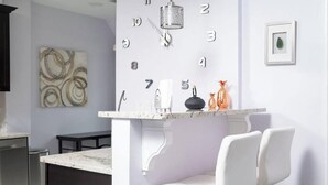 A kitchen with a central island, white bar stools, a clock, and a framed picture on the wall. - Stylish 6-Bedroom Home Near Boston – Dual Units, Yard & Parking Included! (Everett)