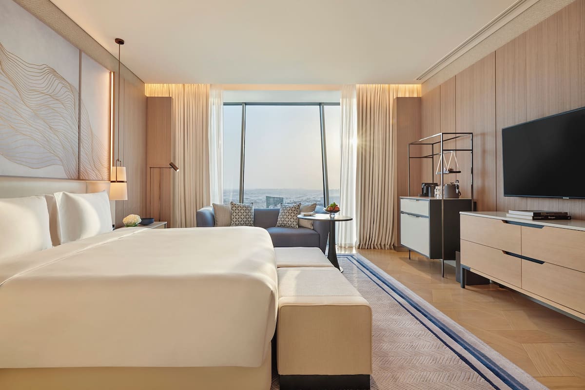 A modern hotel room with a large bed, a desk, a television, and a view of the city.