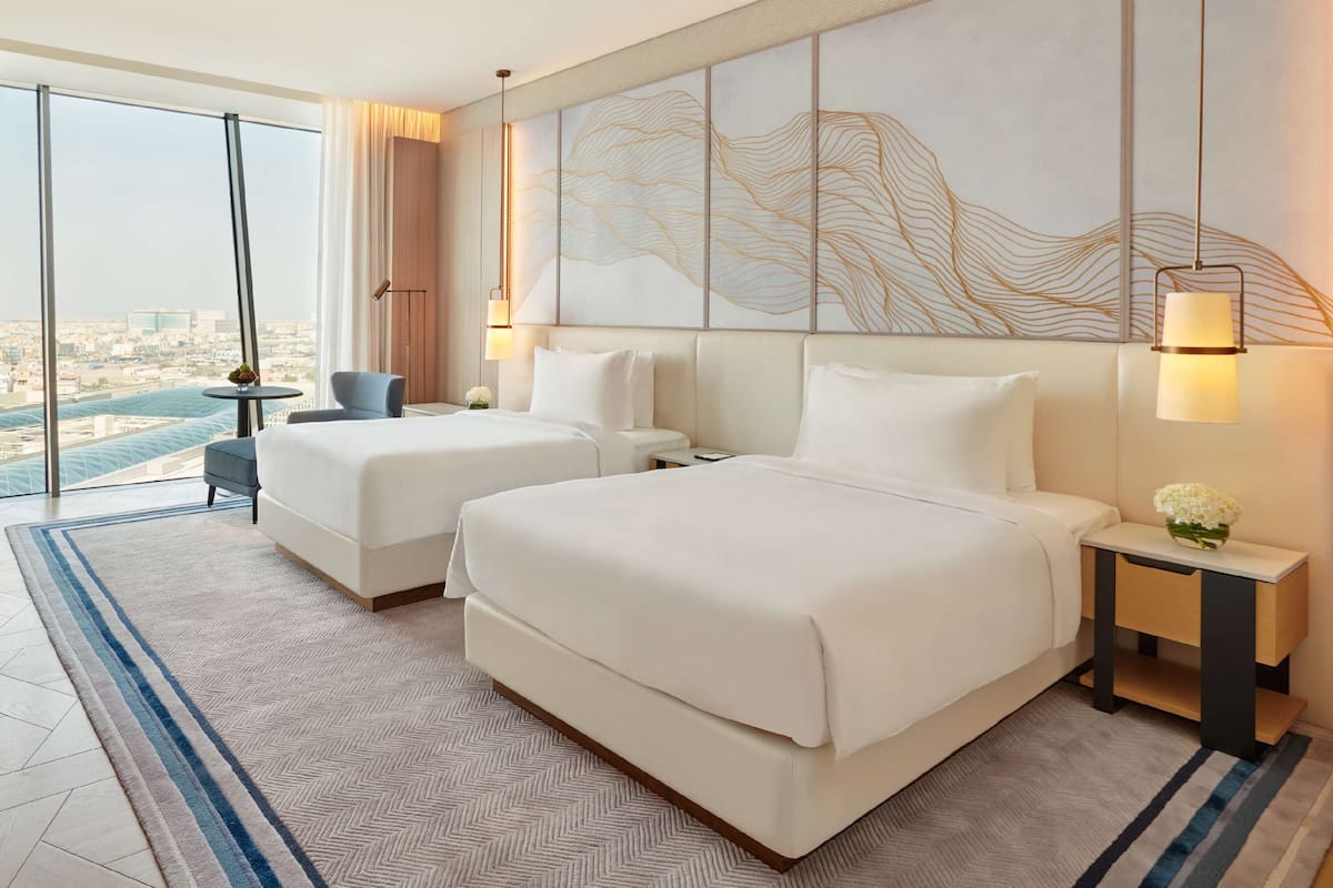 A hotel room with two beds, a view of the city, and a large abstract painting on the wall.
