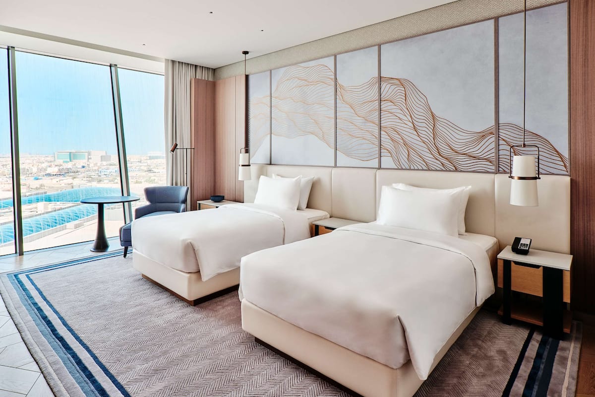 A modern hotel room with two beds, a view of the city, and a large window.
