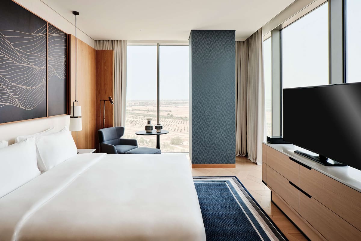 A modern hotel room with a large bed, a TV, a desk, and a view of the city.