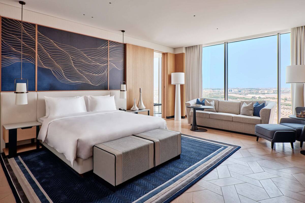 A modern hotel room with a large bed, a sofa, a small table, and a view of the desert.