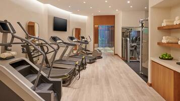 Una palestra moderna con tapis roulant, macchinari per pesi e uno schermo televisivo.