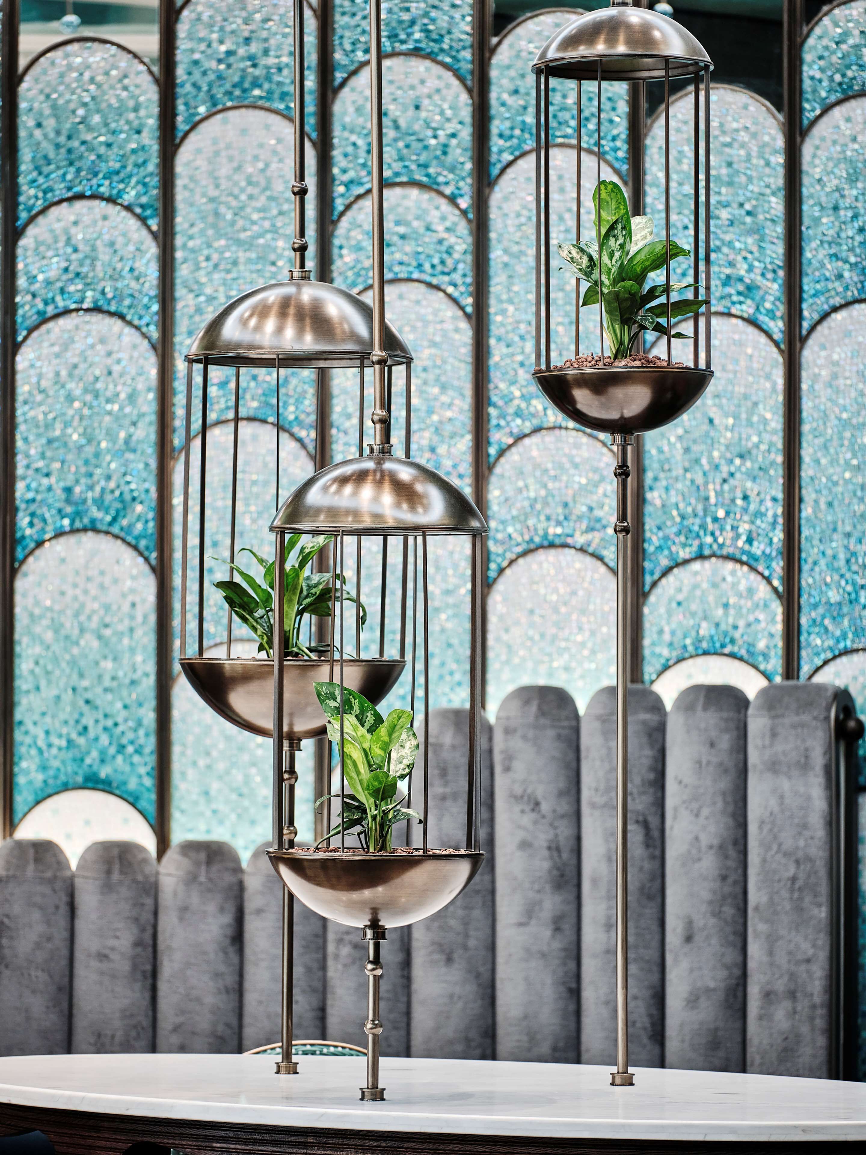 Un jardinier en métal à plusieurs niveaux, orné de plantes, est placé devant un mur décoratif recouvert de carreaux.