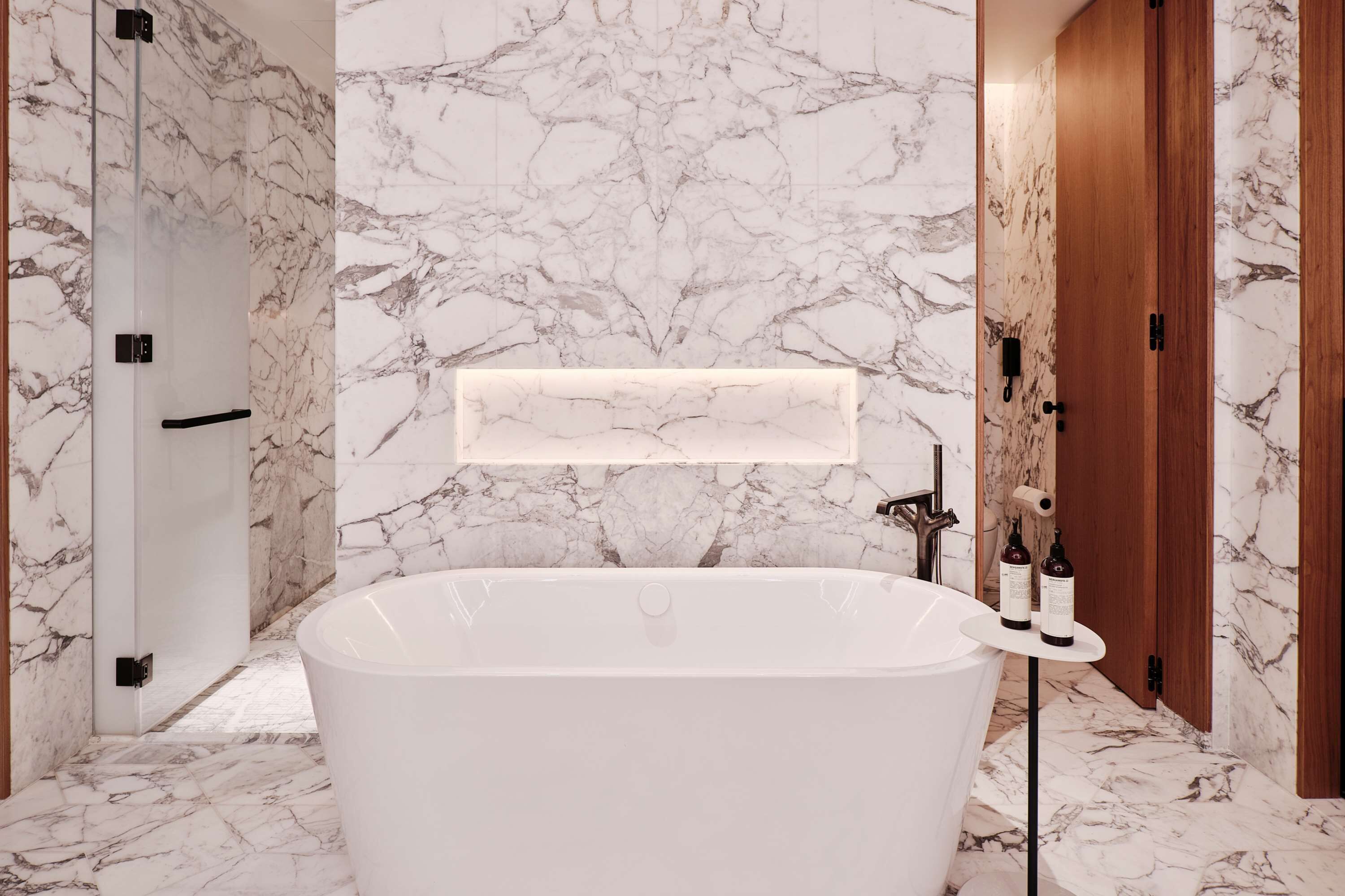 Un baño moderno con una bañera independiente, paredes de mármol y una puerta de madera.