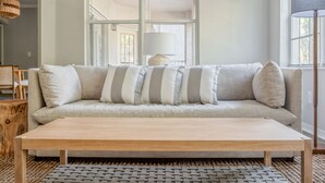 Un sofá de tonos neutros con cojines a rayas, una mesa de centro de madera y una alfombra tejida.